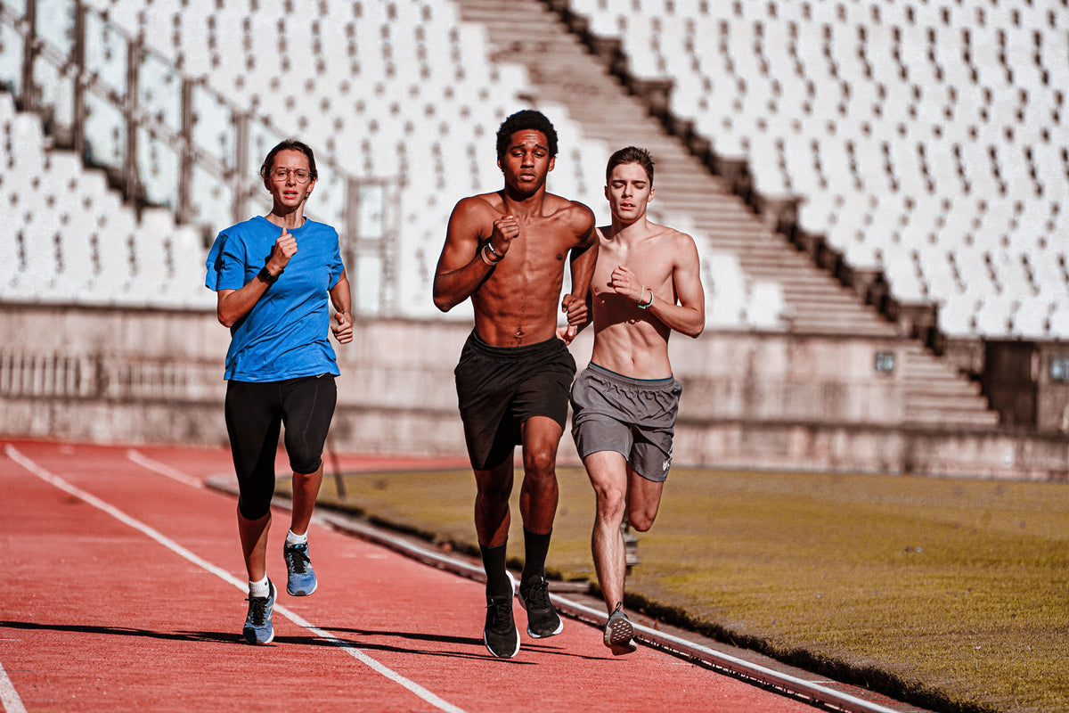 Three people running on a red track in a stadium, showcasing teamwork and physical fitness.